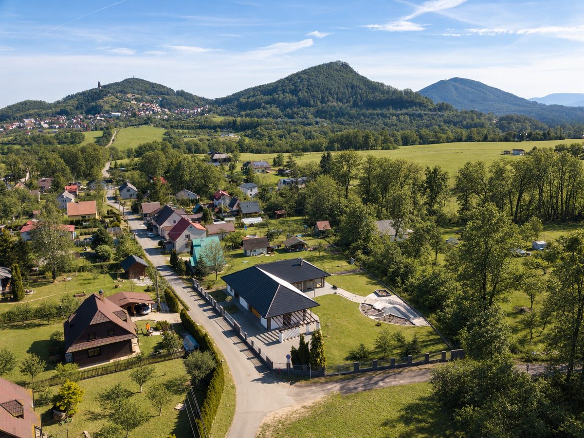 Letecký pohled na Libotín, dům u silnice, v pozadí zalesněné kopce a věž Trúba